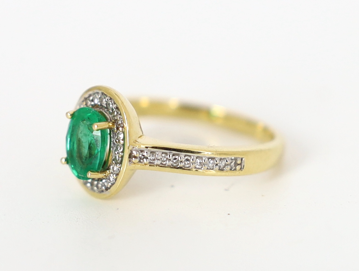 A modern 18ct gold, emerald and diamond set oval cluster ring, with diamond chip set shoulders